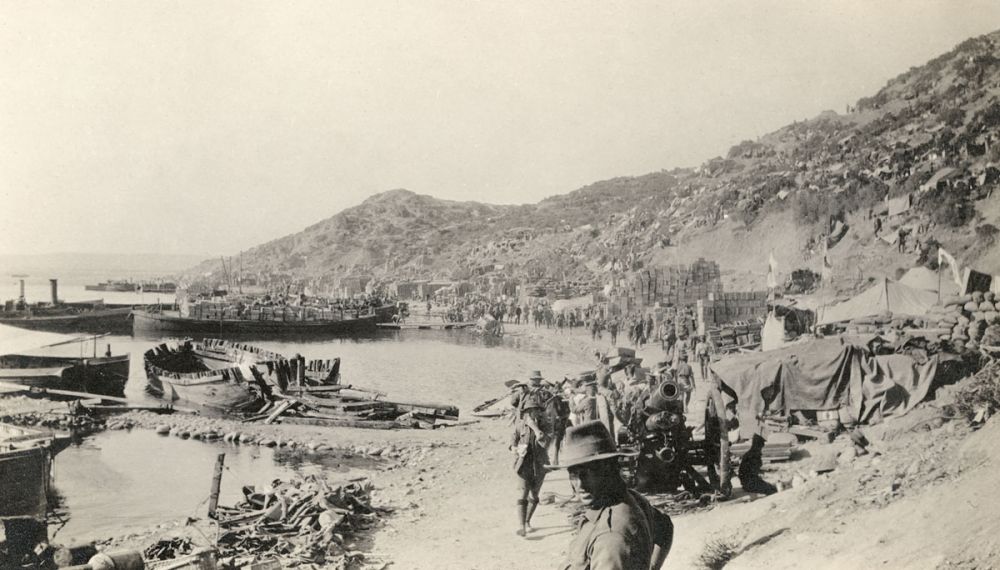 Anzac Cove soon after the landing.  A howitzer and several broken rifles are in the foreground; white flags on the right mark the Casualty Clearing Station.